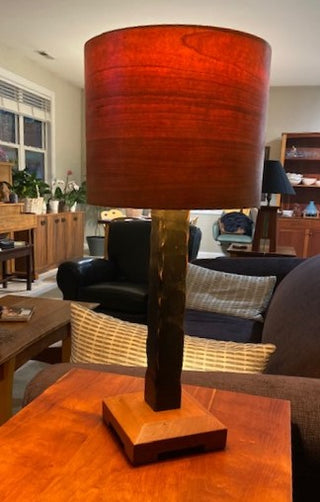 Black Cherry Lamp, handcrafted wood lamp with cherry base, distressed black column and cherry veneer wooden cylinder drum shade. On accent table in living room.