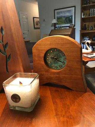 Wooden bell-shaped clock made from sustainable Appalachian Cherry with round green patina copper face, pictured in home with candle in front. American Liberty Mantel Clock