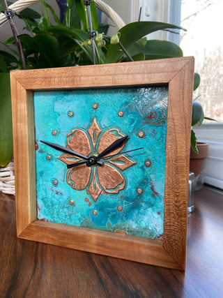 Patina Dogwood, handcrafted cherry wooden Box Clock with patina copper face embossed with a dogwood blossom. Pictured on wooden surface with plants.