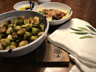 Large white serving bowl with cobalt blue accent lines, on dinner table with Brussels sprouts.