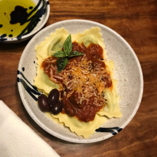 Medium white pasta bowl with cobalt blue accent lines filled with ravioli, red sauce, & parmesan.