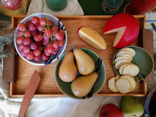 Cherry wood tray with walnut handles laden with fruit, cheese, and crackers on set table.