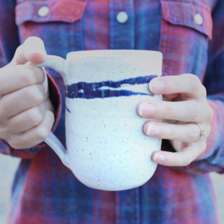Woman in flannel holding with both hands white mug with cobalt blue accent lines.